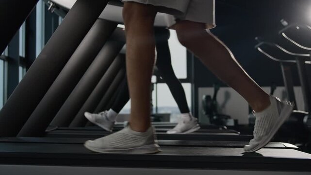 Side view female and male legs walking on treadmill in fitness gym sports shoes slow cardio workout unknown runners moving feet on running machine athletic people healthy lifestyle exercise stride
