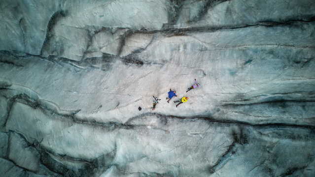 Aerial view of hikers trekking across the textured surface of a glacier with deep crevasses in Iceland.
