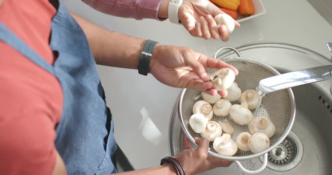 Pair of hands are cleaning mushrooms at sink while faucet is being turned on for cooking