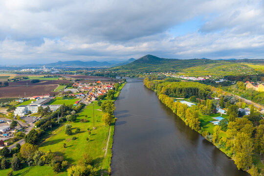 Aerial view of the Labe river flowing through the landscape with green fields, trees, and distant hills under a cloudy sky in Litomerice, Usti nad Labem Region, Czechia.