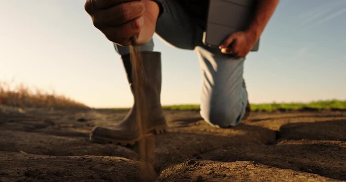 Agricultural specialist checking soil quality on a cracked, arid field. Male hand pouring dry ground, concept of drought and climate change