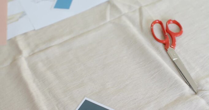 Camera is panning upward and left to reveal fashion illustration sheets and red-handled scissors