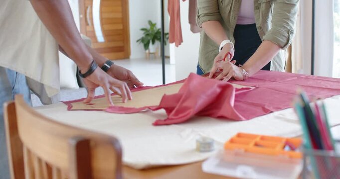 African American colleagues laying pattern on red fabric, cutting with scissors for sewing at table