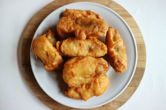 Traditional fried banana with a golden, crispy looking batter coating, served on a white plate.