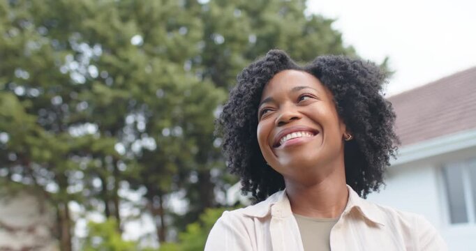 Adult African American woman looking up reacting with widening smile by house trees wearing tan top