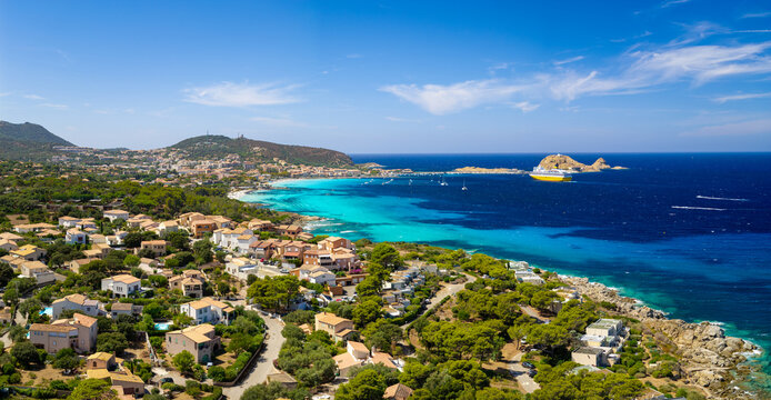 Ile Rousse Cap Corse Corsica drone panorama photo. Yellow ferry approaching bay with red island rocks beaches and villas. High resolution Mediterranean sea travel aerial stock print