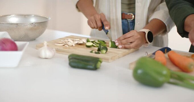 Knife touching zucchini is starting hands who're slicing and peeling carrots on counter for dinner