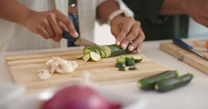 Knife descending as hands are steadying zucchini and slicing rounds on wooden board, preparing meal