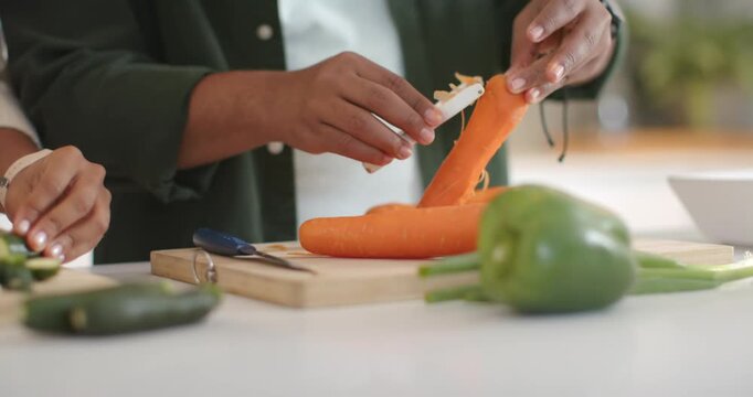 Two hands are peeling carrot as peeler is touching skin, rotating on cutting board, prepping meal