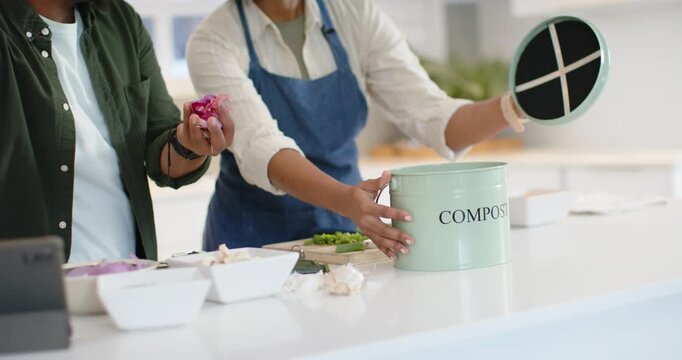African couple prepping meal at island, woman opening mint compost can as man pressing onion scraps
