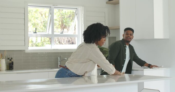 African American couple cleaning kitchen island, woman wiping holding spray bottle, man joining