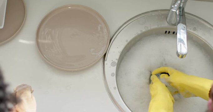 Seeing soapy sink, African American couple washing plates at sink in yellow gloves with sponge