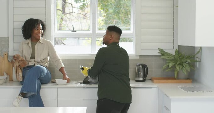 African American couple at sink, woman reaching bowl tossing sponge, man in yellow gloves washing