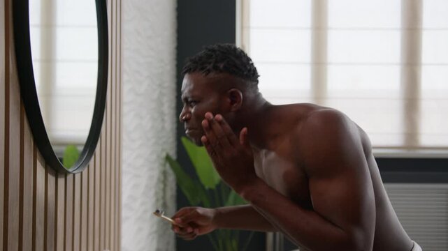 Upset African American man brushing white teeth with toothbrush in home bathroom suffering male guy bleeding tooth toothache pain sensitive gums periodontitis caries oral cavity ache morning hygiene