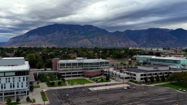 Orem, Utah - 30 August 2026: Aerial view of the UVU campus featuring modern academic buildings, green courtyards, and the Wasatch Range mountains under a cloudy sky.