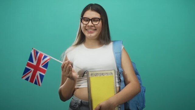 Young woman holds uk flag in hand and clutches books with bare midriff visible in studio; study abroad pride.