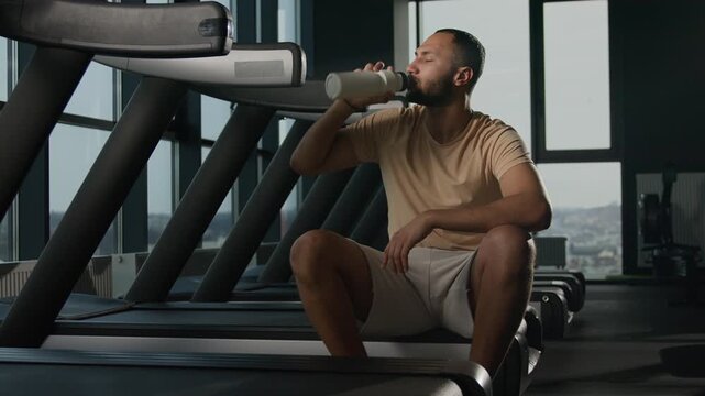 African American sportsman drinking water after treadmill workout in fitness gym exhausted runner male man hydrating sports bottle tired athlete resting cardio training protein drink thirst recovery