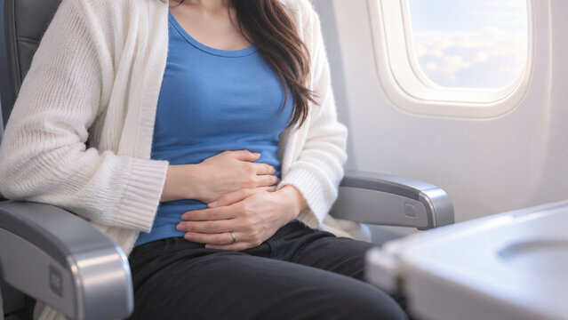 Female Passenger Holding Stomach in Airplane Seat Experiencing Abdominal Pain, Motion Sickness and Travel Discomfort During Flight
