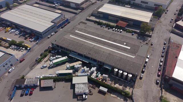 San Giuliano Milanese, Italy - 05 September 2026: Aerial view of an industrial zone featuring large warehouse buildings, storage tanks, parked trucks, and cars on asphalt roads.