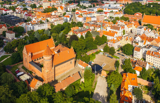 Aerial view of the historic Castle of the Warmian Chapter with red-tiled roofs and a tall tower, surrounded by green parkland and urban architecture in Olsztyn, Warmian-Masurian Voiv, Poland.