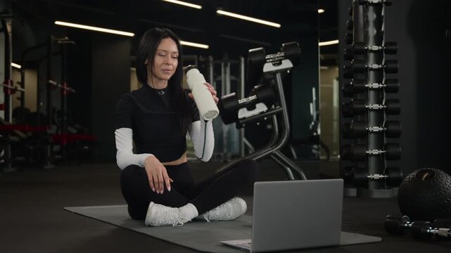 Smiling Caucasian woman fitness instructor teaching online workout with laptop in gym happy female sportswoman showing thumb up drinking water after exercise athletic trainer yoga pilates video class