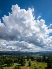 Obraz premium Fluffy white cumulus clouds over a green valley landscape on a bright sunny summer day