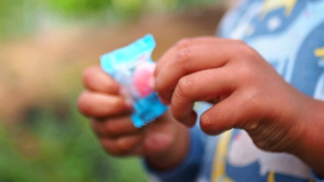 Close-up of Child's Hands Unwrapping Pink Candy from Blue Package