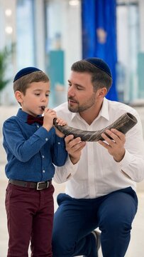 Jewish boy blowing ram horn beside his father in synagogue, yom kippur observance, childhood participation in sacred holiday ritual
