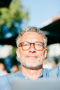 Portrait of Confident Mature Man with Gray Curly Hair and Glasses Outdoors in Summer