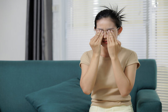 Women wearing eyeglasses rubbing her irritated eye, representing strain, tired eyes, discomfort, vision care, fatigue, healthcare, common irritation symptoms.