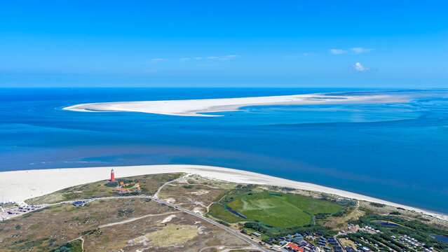 Aerial view of the red Eierland Lighthouse on the sandy dunes of Texel island, surrounded by the Wadden Sea and the island Vlieland under a clear blue sky in Texel, North Holland, Netherlands.