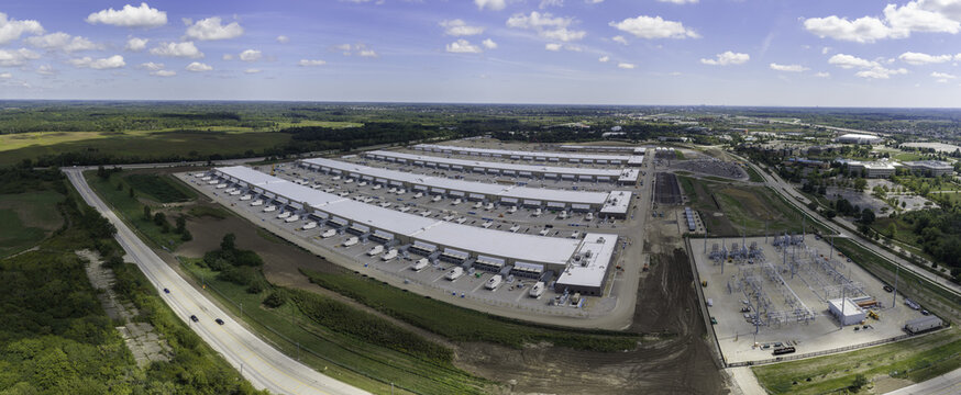 Aerial view of a large industrial data center complex with long buildings, loading docks, and an electrical substation near green fields in Hoffman Estates, Illinois, United States.