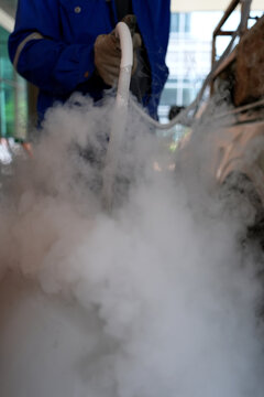 Liquid nitrogen, vapor, cryogenic, hose, worker, glove mist surrounds cryogenic hose during industrial handling with cold fog near equipment in indoor facility