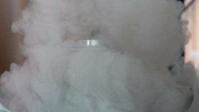 Liquid nitrogen vapor fog cryogenic smoke white cloud mist near laboratory equipment dewar flask cold gas plume dense indoor science container metal valve low visibility soft light atmosphere