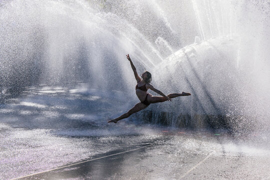 White woman performing a graceful dance leap through water fountain