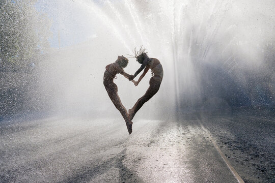 Two white women jumping hand in hand under water spray outdoors