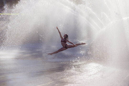 White woman performing a split leap through water spray