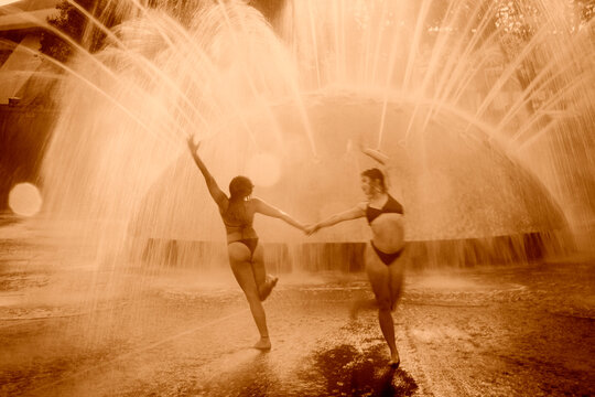 Two white women dancing and practicing acrobatics under fountain water