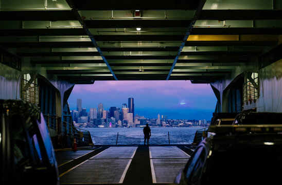 White person on ferry deck viewing city skyline at twilight