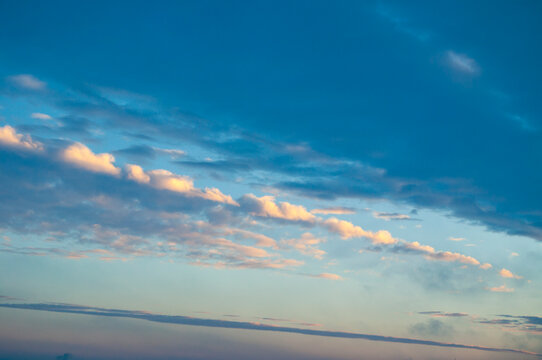Dramatic sunset sky landscape with horizontal bands of clouds. Golden sunlight illuminating the cloud edges and a soft hazy horizon