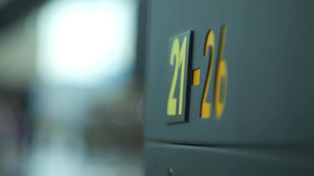 Close-up of airport gate sign showing numbers 21-26 in yellow. Background blurred with soft lighting. Focus on signage details for travel or transit scenes