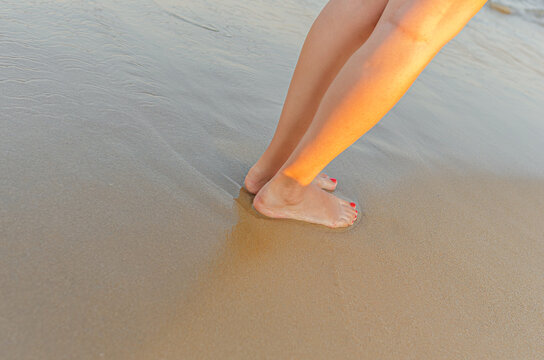 A woman stands barefoot on the wet sand of a tropical beach during golden hour.