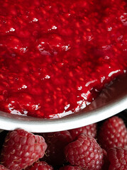 Close-up of fresh raspberry jam pouring from a metal bowl, with ripe raspberries in the foreground. Full frame texture © Наталья Бабак