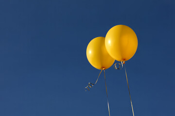 Obraz premium Two Yellow Balloons Flying Against Clear Blue Sky Background