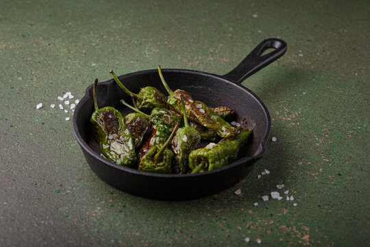Padron peppers fried cast iron skillet sea salt dark green background Spanish appetizer