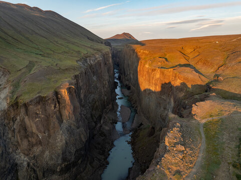 Aerial view of a deep canyon with a river flowing through steep rocky cliffs under golden hour light in Iceland.