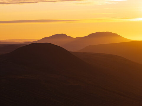 Aerial view of rolling hills and mountains at sunset with golden light casting long shadows over the landscape, Iceland.