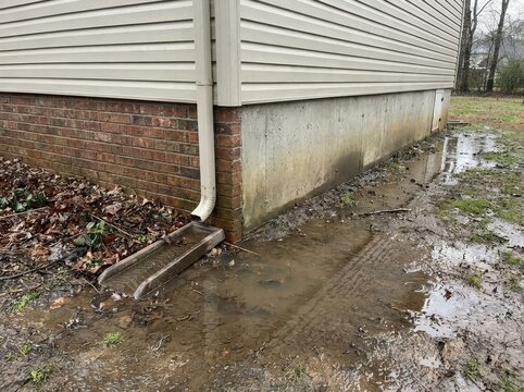 flood risk Corner of a house with water pooling from a downspout onto wet ground.