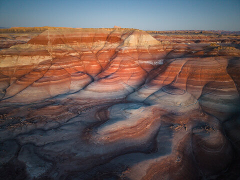 Aerial view of the colorful striped landscape of the Hanksville Bentonite Hills with layered sedimentary rock formations under a clear sky in Hanksville, Utah, United States.