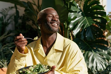 Obraz premium Smiling man eating salad in indoor tropical greenery for healthy lifestyle food background and wellness banner